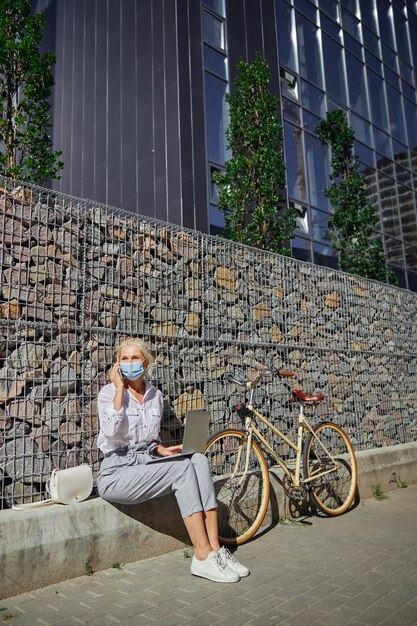 Portrait complet d'une femme d'affaires avec un vélo rétro près d'elle travaillant sur l'ordinateur portable dans une ville urbaine