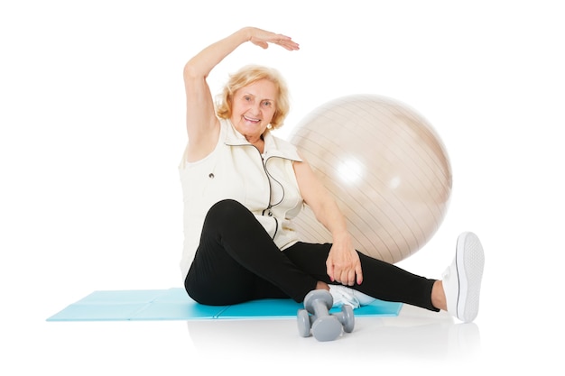 Portrait complet d'une femme âgée faisant des exercices d'étirement assis sur un tapis isolé sur fond blanc