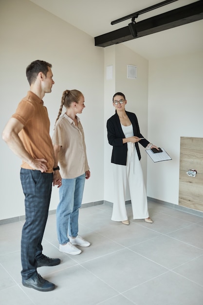 Portrait complet d'une femme agent immobilier donnant une visite d'appartement à un jeune couple achetant une nouvelle propriété