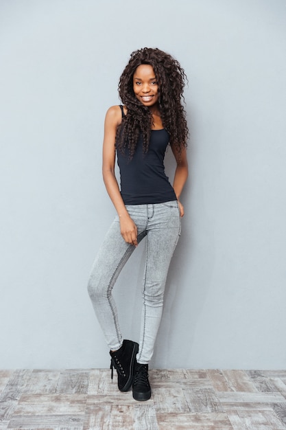 Portrait complet d'une femme souriante debout sur un mur gris