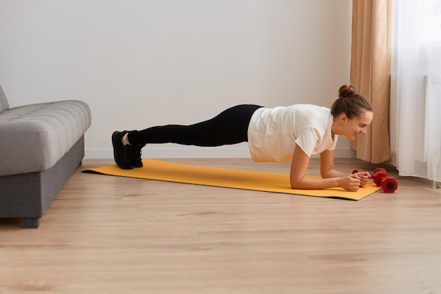 Portrait complet d'une femme sportive faisant de l'exercice, debout sur une planche, entraînant ses abdominaux, son endurance et sa force sur un tapis de yoga, un mode de vie sain, une forme physique et un entraînement à la maison.