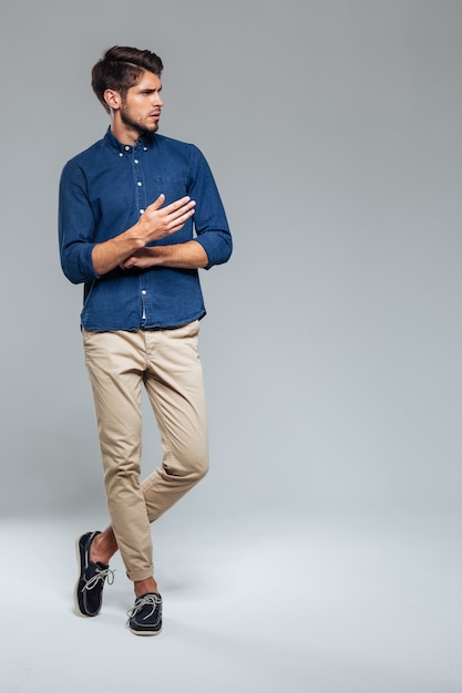 Portrait complet d'un homme décontracté debout avec les jambes croisées sur un mur gris