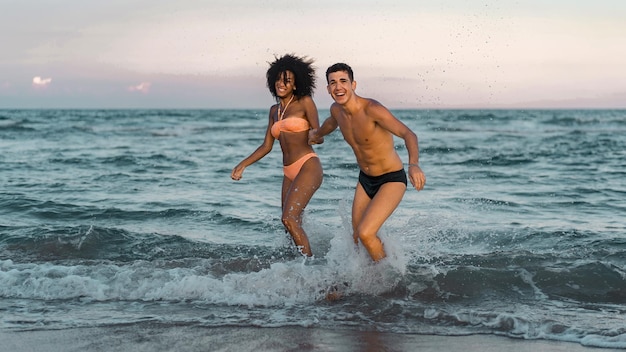 Portrait complet d'un jeune couple interracial s'amusant à se détendre sur la plage, main dans la main sur l'eau Concept amusant d'été