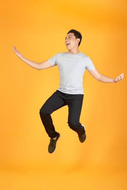 Portrait complet d'un jeune homme excité en t-shirt blanc sautant tout en célébrant le succès isolé sur fond orange