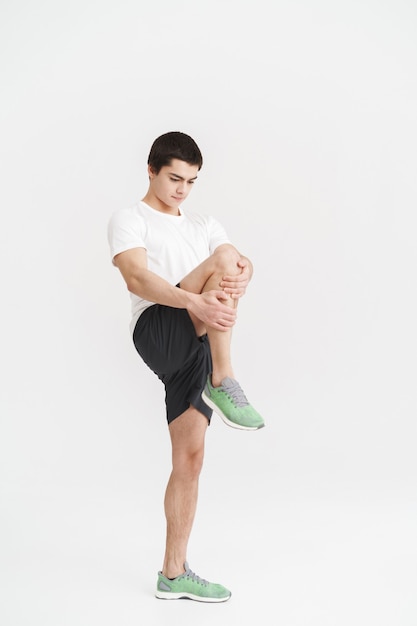 Portrait complet d'un jeune sportif en bonne santé s'échauffant avant de faire du jogging isolé sur un mur blanc