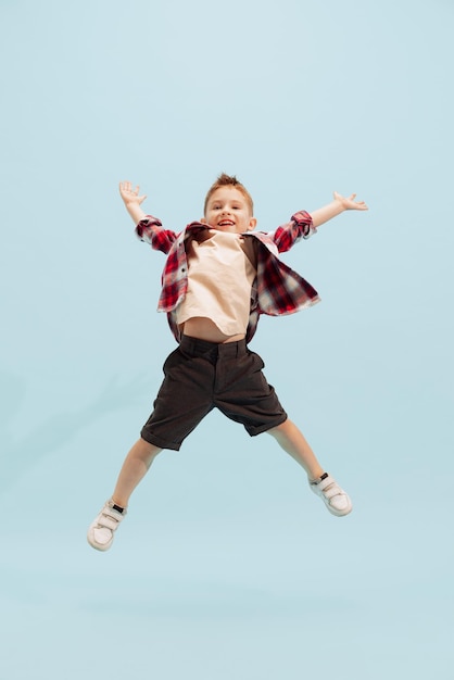 Portrait complet d'un petit garçon enfant sautant joyeusement opsing isolé sur fond bleu