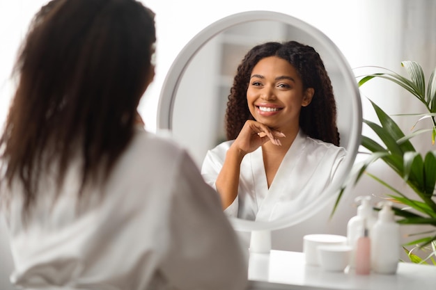 Portrait de concept de beauté d'une jolie femme noire regardant dans un miroir à la maison