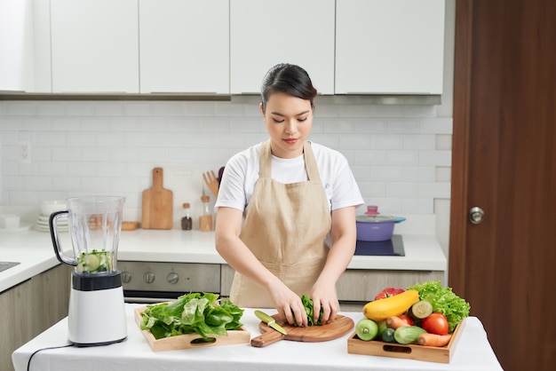 Portrait de concept de mode de vie sain d'une belle jeune femme préparant une boisson avec des légumes et des verts.