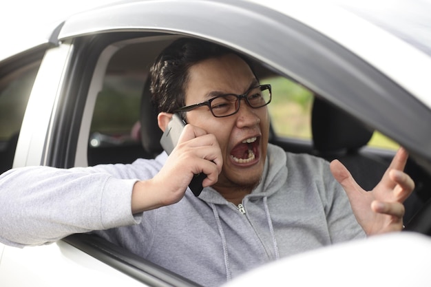 Photo portrait d'un conducteur asiatique qui crie en parlant au téléphone. un homme en colère qui reçoit de mauvaises nouvelles.