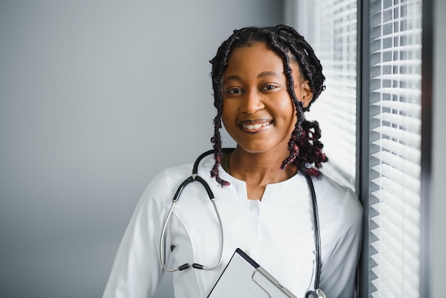 Portrait confiant femme médecin africaine professionnel de la santé écrivant des notes de patient isolées sur fond de fenêtres de couloir de clinique d'hôpital Expression positive du visage