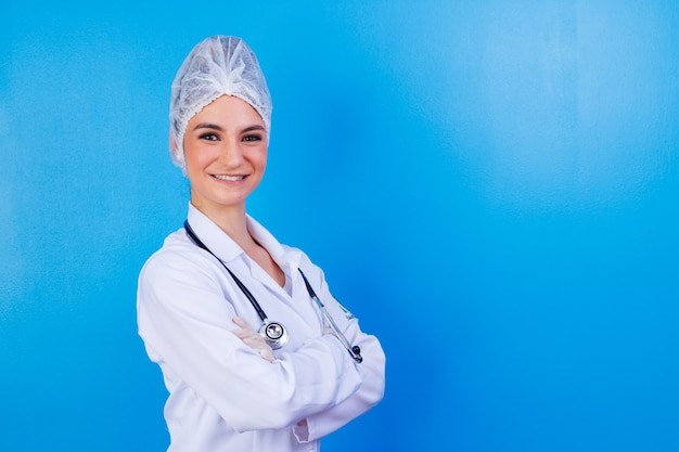 Portrait de confiant avec un sourire rayonnant à pleines dents qualifié médecin intelligent intelligent et expérimenté portant des vêtements de cérémonie blancs, elle se tient debout avec les bras croisés croisés, isolée sur fond bleu