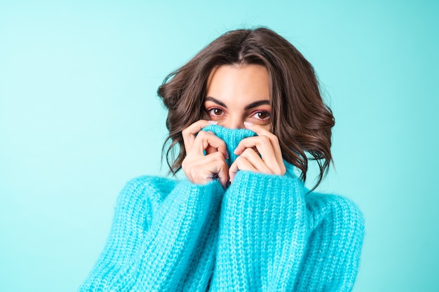 Portrait confortable d'une jeune femme dans un pull bleu tricoté et maquillage rose vif sur turquoise