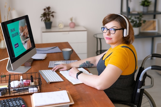 Portrait de contenu jeune femme corpulente dans des écouteurs sans fil assis en fauteuil roulant