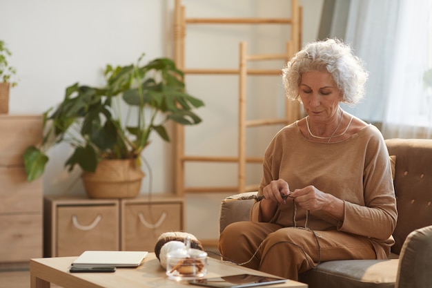 Portrait de contenu senior woman knitting in cosy home éclairé par la lumière du soleil