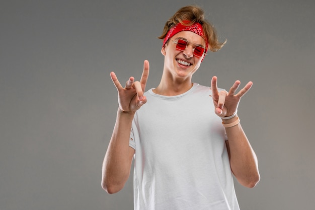 Un portrait de cool young caucasian man with short red curly hair in white t-shirt, red glasses show a doigts isolated on a grey