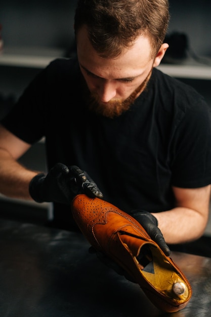 Portrait de cordonnier en gants noirs frottant la peinture sur l'orteil de chaussures en cuir marron avec les doigts