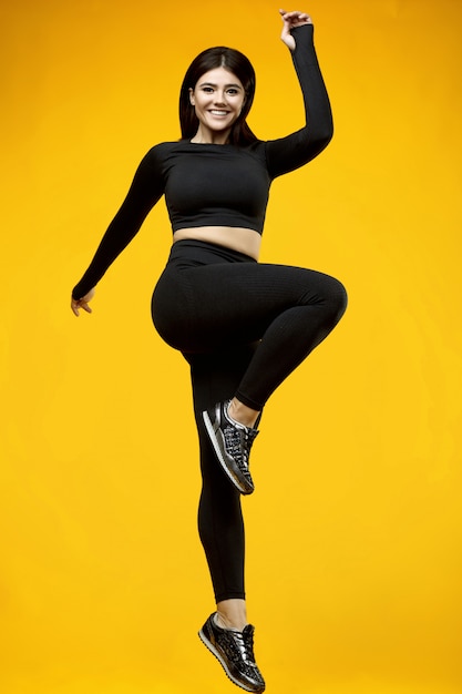 Portrait d'un corps magnifique femme latine positive dans un costume de sport noir exerçant sur jaune