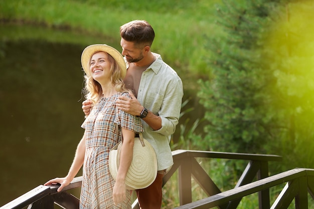 Portrait de couple adulte romantique souriant joyeusement en marchant sur le pont de bois au bord du lac dans un paysage rustique