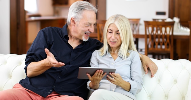 Portrait d&#39;un couple d&#39;âge mûr souriant à l&#39;aide de tablette numérique sur un canapé à la maison