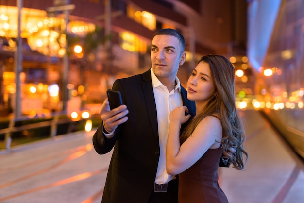 Portrait de couple à l'aide de téléphone à l'extérieur la nuit dans la ville de Bangkok en Thaïlande