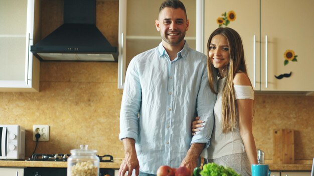 Portrait d'un couple d'amoureux souriant et regardant dans la caméra dans la cuisine à la maison