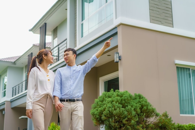 Portrait de couple asiatique marchant et serrant ensemble à la recherche de plaisir devant leur nouvelle maison pour commencer une nouvelle vie. Concept de famille, âge, maison, immobilier et personnes.