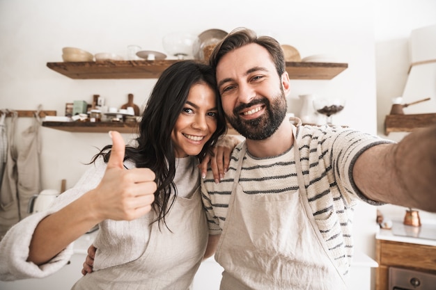 Portrait d'un couple caucasien homme et femme portant des tabliers prenant une photo de selfie pendant la cuisson dans la cuisine à la maison