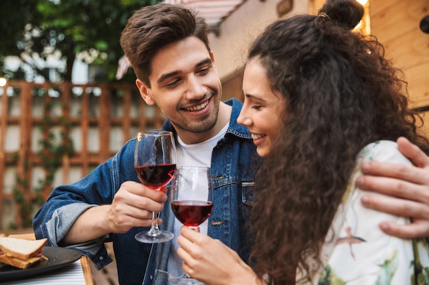 Portrait de couple charmant homme et femme buvant du vin rouge tout en s'embrassant près de la remorque à l'extérieur