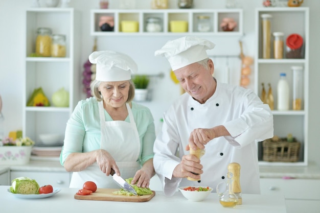 Portrait de couple de chefs seniors souriants à la cuisine