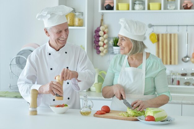 Portrait de couple de chefs seniors souriants à la cuisine