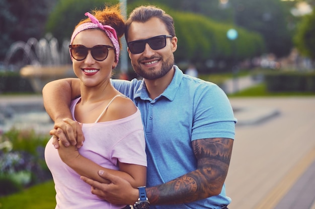 Portrait d'un couple élégant sur la fontaine de la ville. Un homme aux bras tatoués pend une femme rousse.