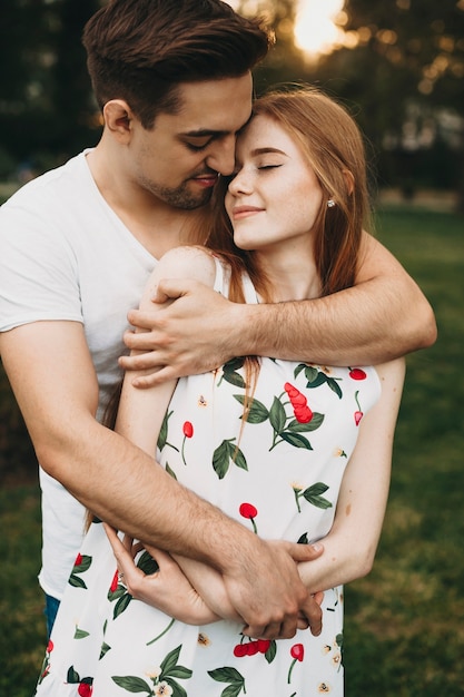 Portrait d'un couple étonnant embrassant les yeux fermés en souriant tout en sortant à l'extérieur contre le coucher du soleil pendant leurs vacances