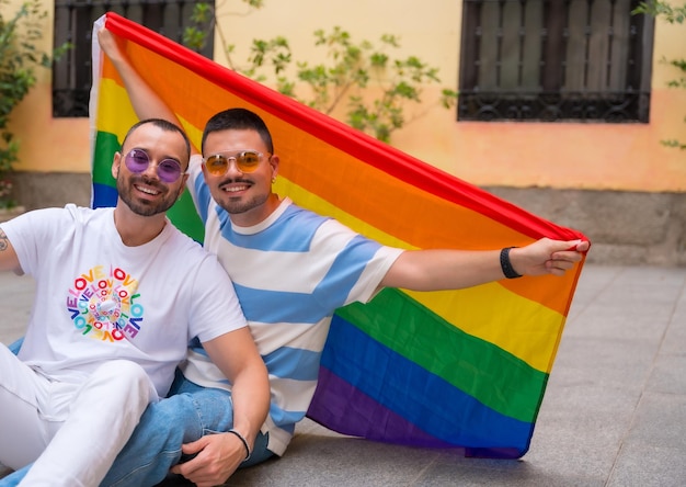 Portrait d'un couple gay assis sur le sol avec un drapeau arc-en-ciel au concept lgbt de la fête de la fierté