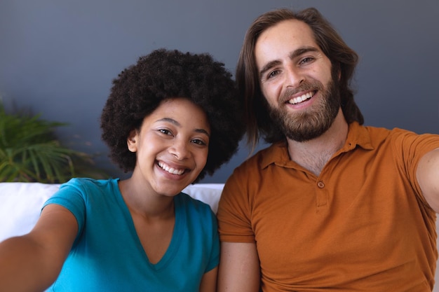 Portrait d'un couple heureux et diversifié assis sur un canapé embrassant et souriant