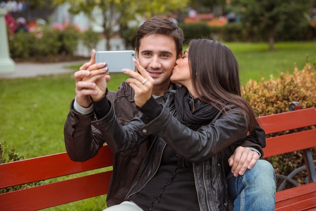 Portrait d'un couple heureux faisant selfie photo sur le banc à l'extérieur