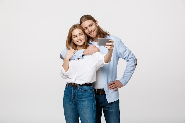 Portrait d&#39;un couple heureux faisant selfie photo avec smartphone sur studio blanc isolé