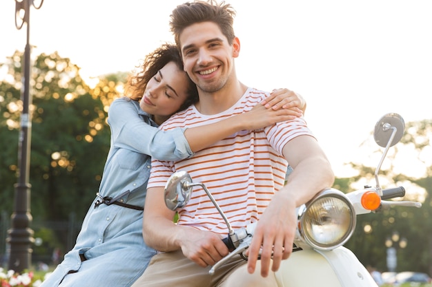 Portrait de couple joyeux, souriant et serrant ensemble alors qu'il était assis sur une moto dans le parc de la ville