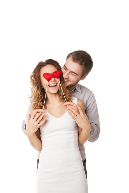 Portrait d'un couple joyeux tenant des coeurs rouges par les yeux et riant