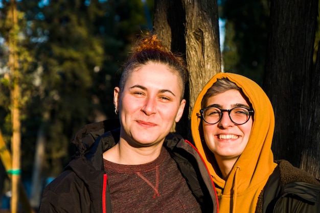Portrait de couple lesbien gay, deux femmes adultes dans le parc, souriant et serrant, heure du coucher du soleil
