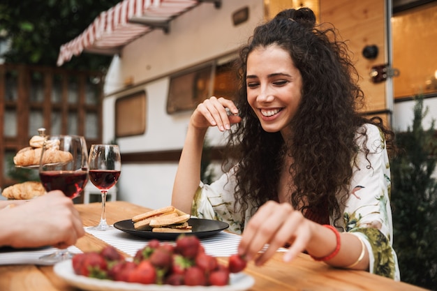 Portrait de couple mignon homme et femme buvant du vin rouge tout en mangeant des fraises ensemble à une table en bois à l'extérieur