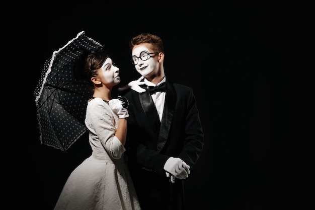 Portrait de couple mime avec parapluie sur fond noir. homme en smoking et lunettes et femme en robe blanche. espace pour le texte