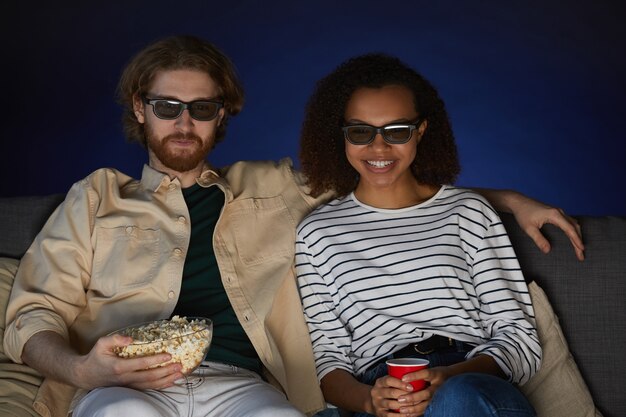 Portrait de couple moderne métisse regardant un film et portant des lunettes stéréo tout en profitant de la date au cinéma