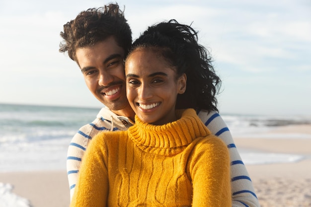 Portrait d'un couple multiracial souriant debout à la plage contre le ciel par une journée ensoleillée