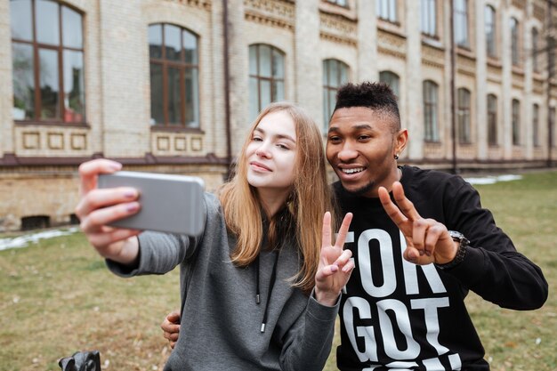 Portrait d'un couple multiracial souriant prenant un selfie et montrant un geste de paix