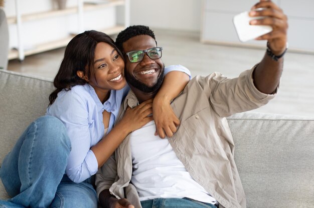 Portrait d'un couple noir heureux prenant selfie ensemble à la maison