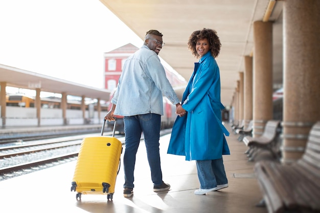 Portrait d'un couple noir romantique marchant avec une valise à la gare