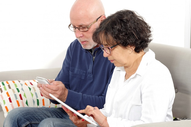 Portrait de couple de personnes âgées à l'aide de tablette et téléphone