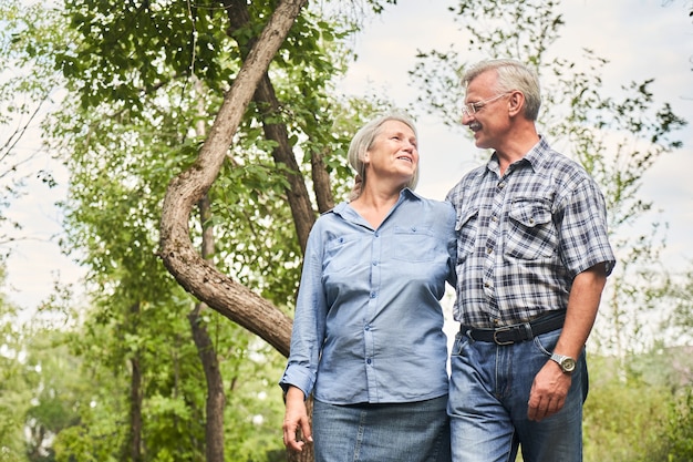 Portrait de couple de personnes âgées amoureux souriant et étreignant dans le contexte des arbres verts