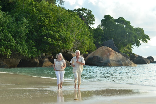 Portrait d'un couple de personnes âgées courant sur une plage tropicale