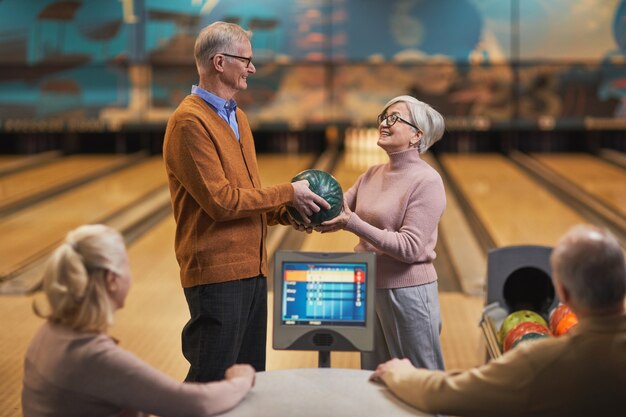 Portrait d'un couple de personnes âgées heureux jouant au bowling avec un groupe d'amis au centre de divertissement, espace pour copie